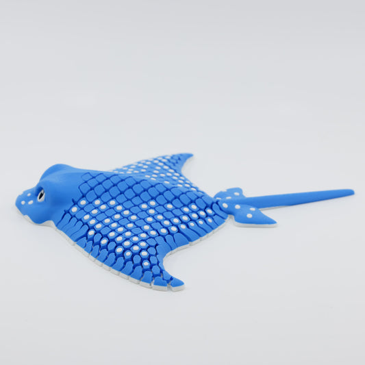 Side view of 3D printed flexible stingray fidget displaying its floppy body and flowing tail in blue