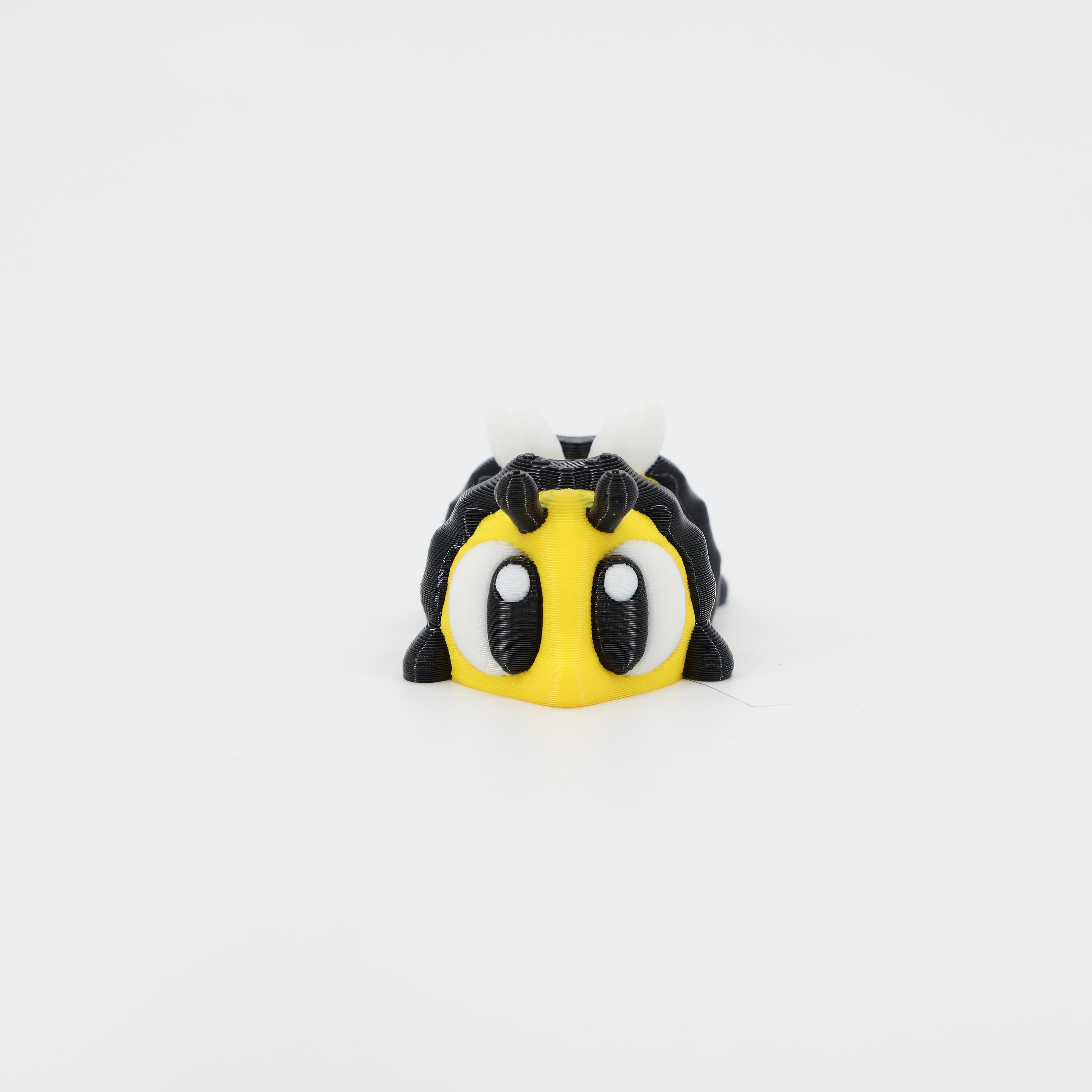 3D printed Bee Wiggle Bud flexible insect toy shown from the front. Features the striped, segmented body and detailed head, a popular articulated critter 3D print.