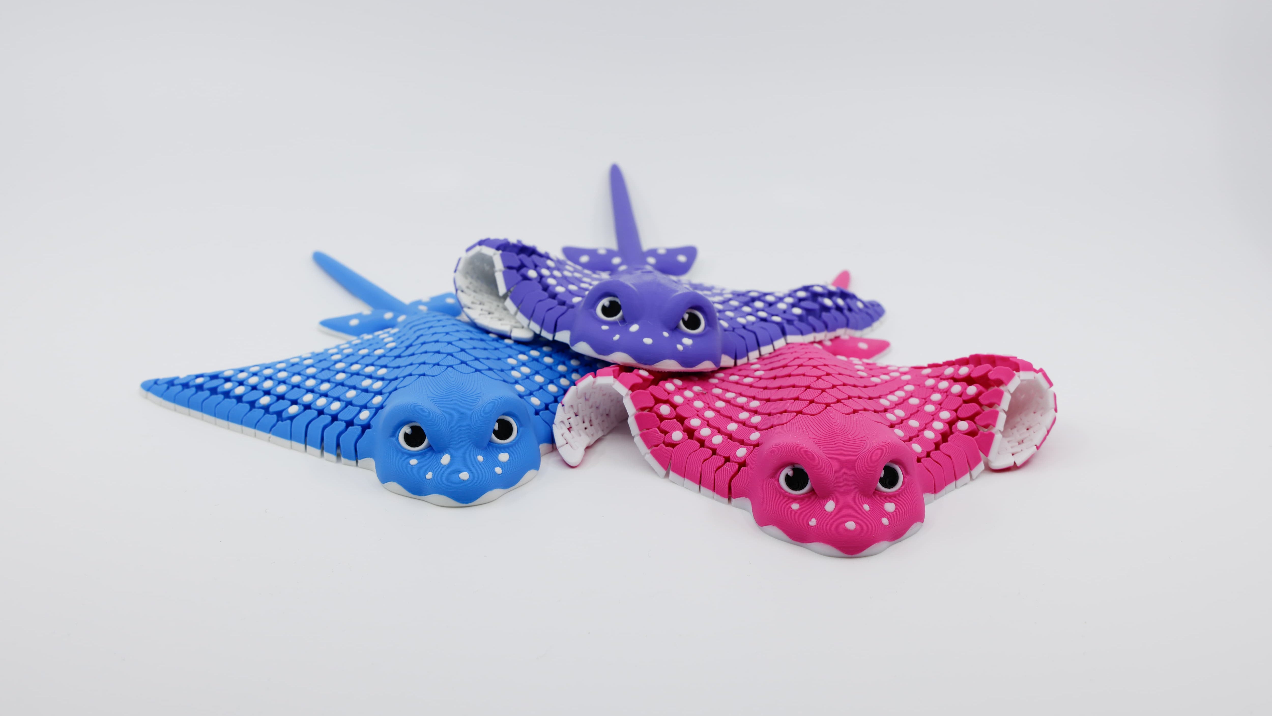 Multiple 3D printed flexible stingray fidgets shown together, demonstrating different angles and motions in blue pink and purple