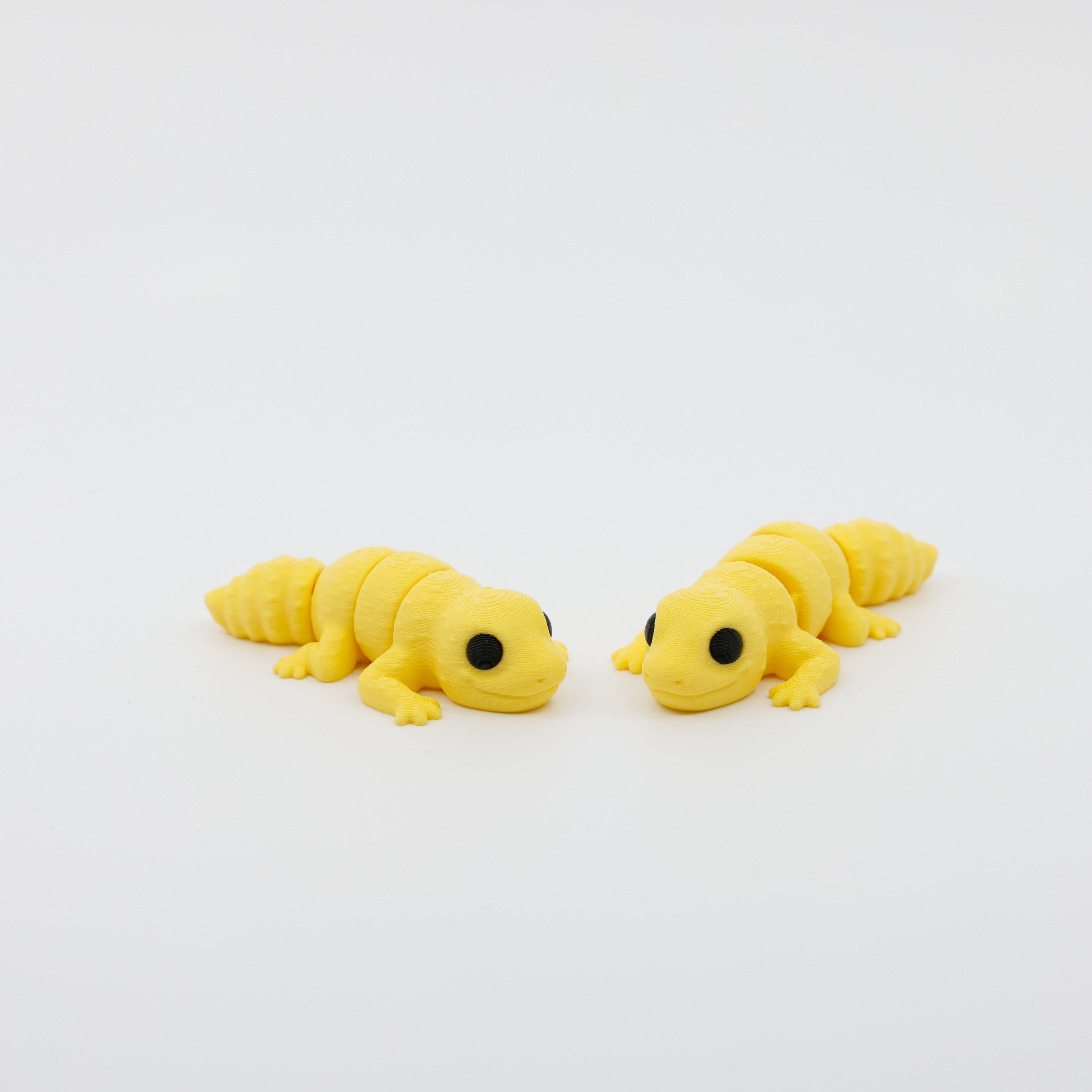Two articulated gecko fidgets displayed side by side, featuring sensory-friendly design and detailed finish