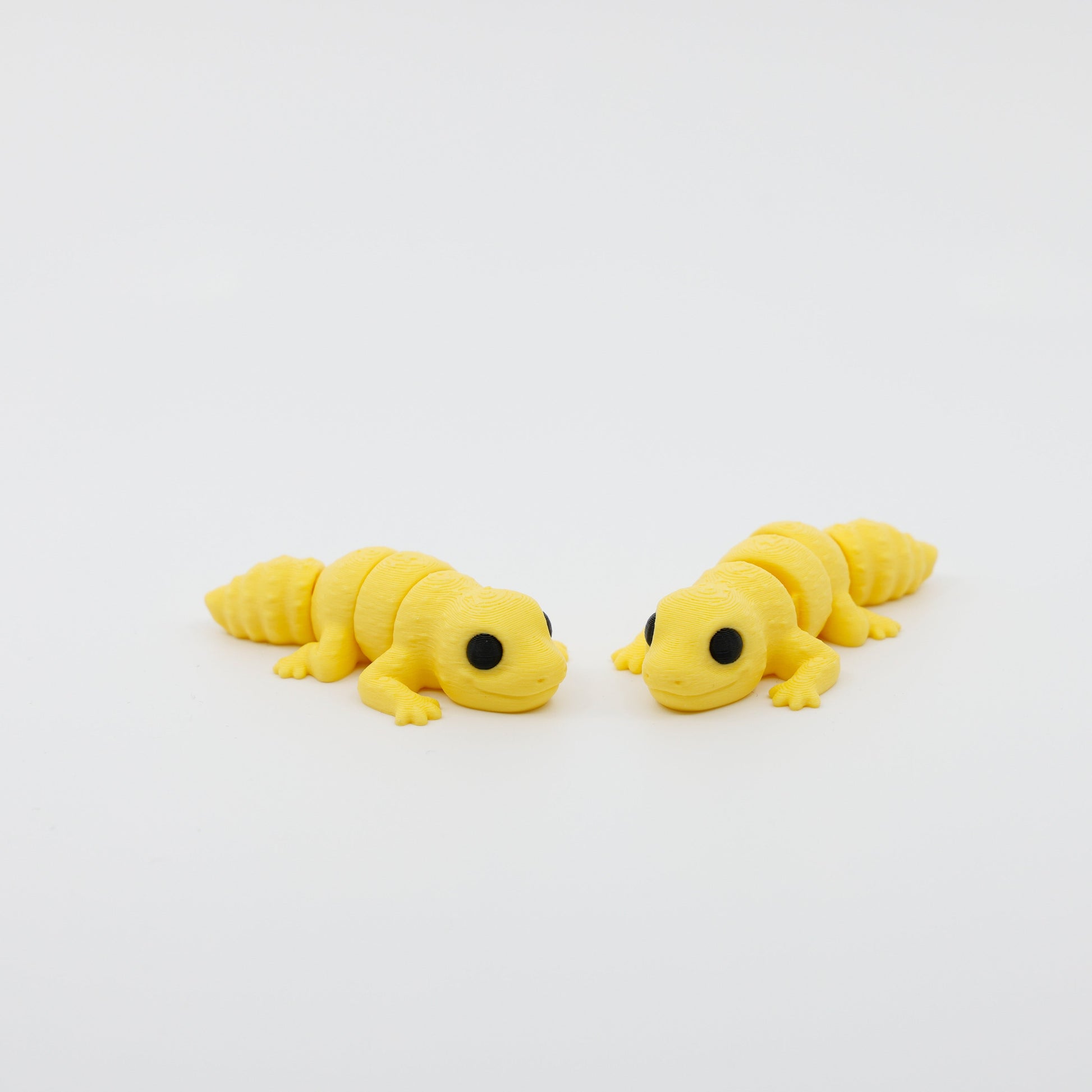 Two articulated gecko fidgets displayed side by side, featuring sensory-friendly design and detailed finish